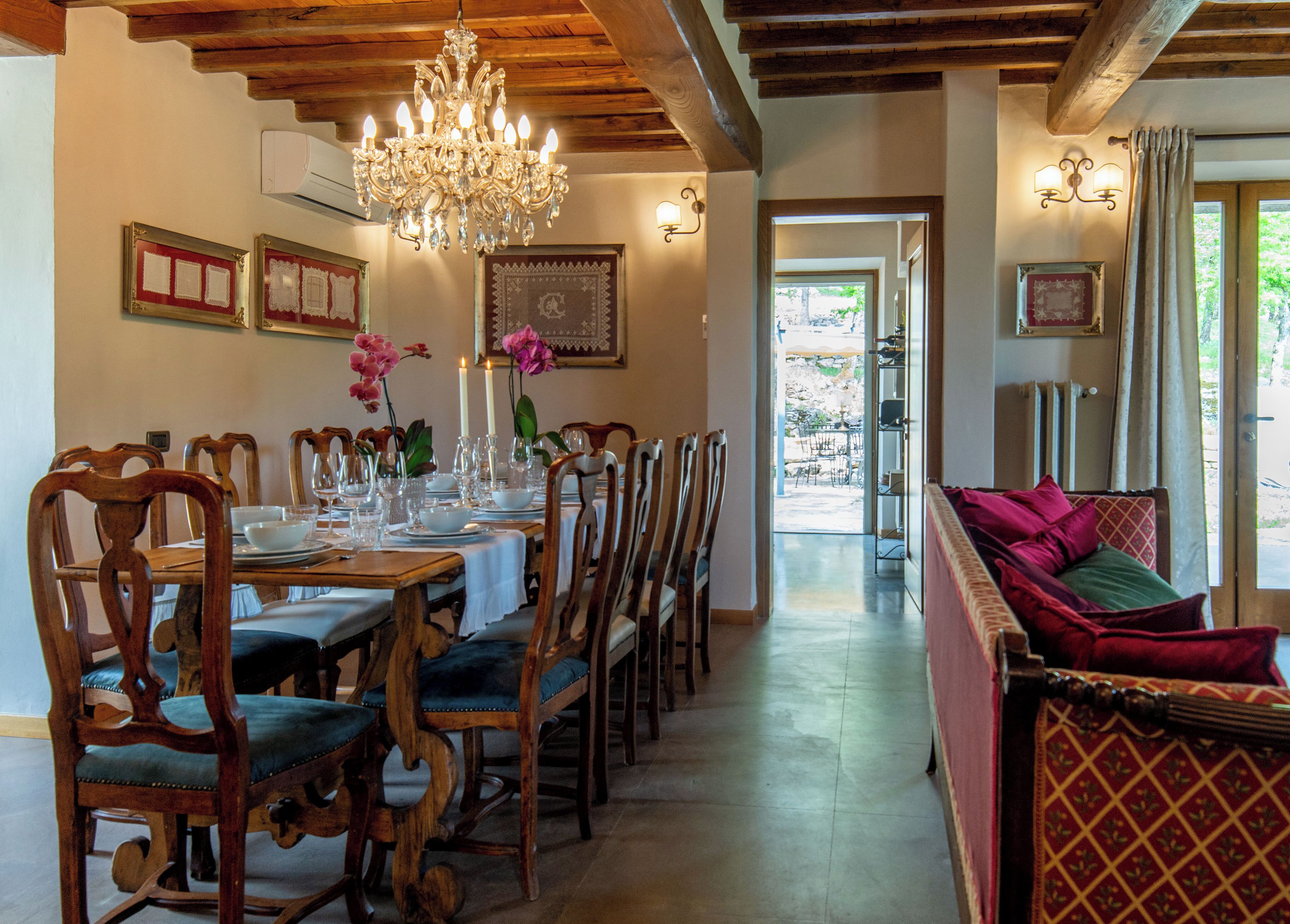 Un comedor con una larga mesa de madera dispuesta para una comida, flanqueada por sillas de madera con asientos acolchados.