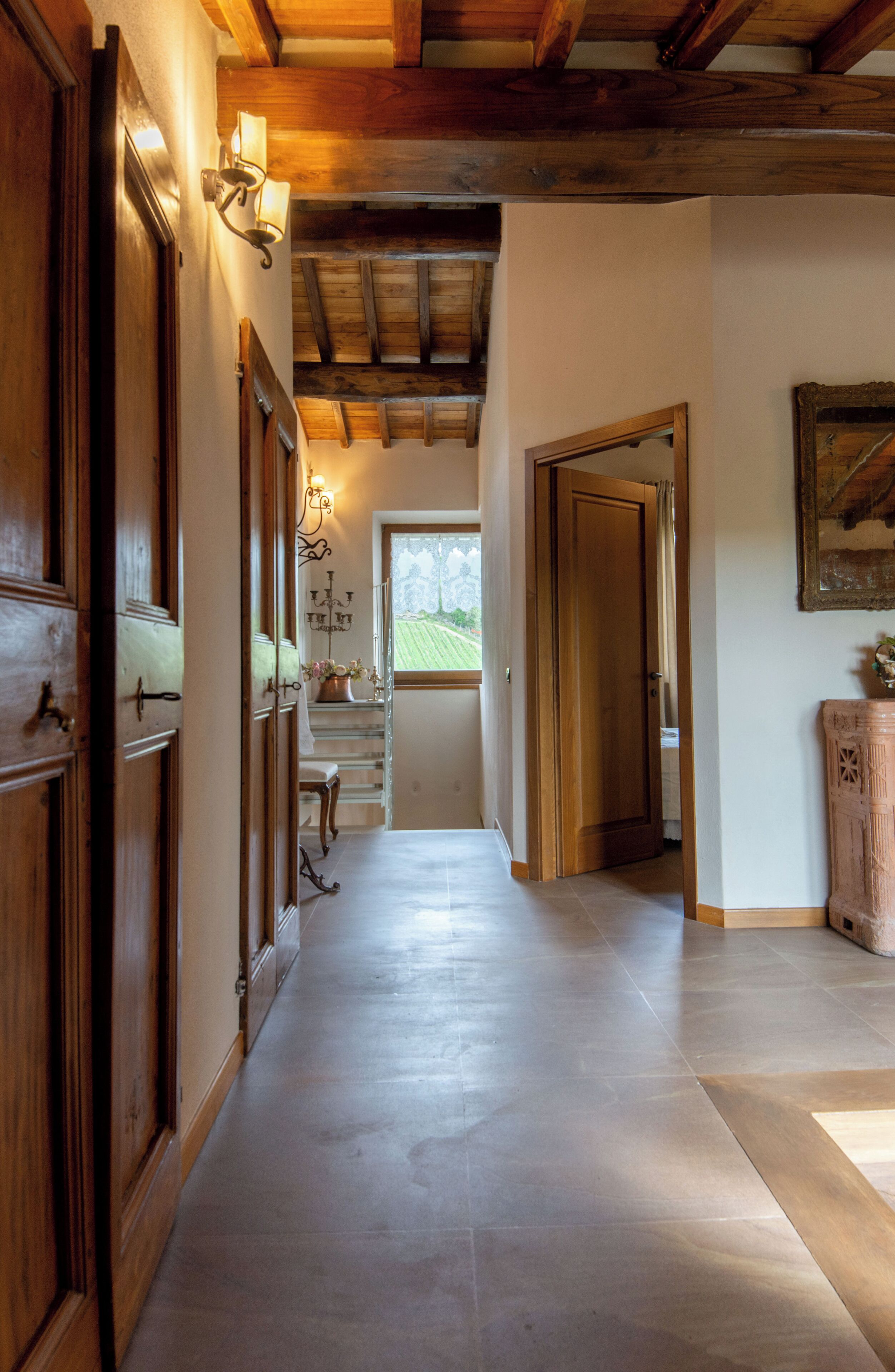 A hallway with wooden doors, a chandelier, and a view of the outdoors.