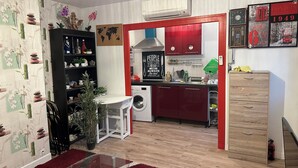 Une cuisine compacte équipée d’un lave-linge, d’un coin repas avec une table en verre et d’un meuble rouge.
