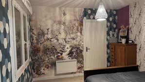 Une chambre à coucher avec une fresque représentant une scène de forêt, un lit, une armoire et un luminaire suspendu.