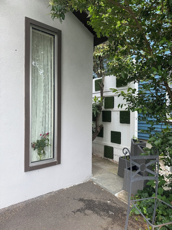 Um edifício branco com uma janela grande, um pequeno alpendre e uma árvore que oferece sombra.