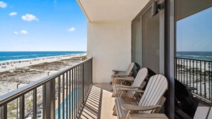 Un balcón con vista a la playa, con tres sillas tipo Adirondack y una mesa.