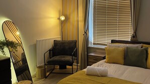 A bedroom with a bed, a chair, a desk, and a window with blinds.