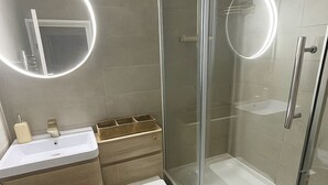 A modern bathroom with a glass-enclosed shower, a toilet, and a sink with a mirror.