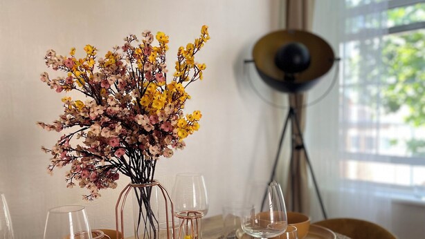 A dining table set with clear glassware, a yellow bowl, and a vase with dried flowers.