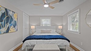 A bedroom with a bed, two bedside tables, a ceiling fan, and a large abstract painting on the wall. - Urban Escape | Near Downtown (Raleigh)