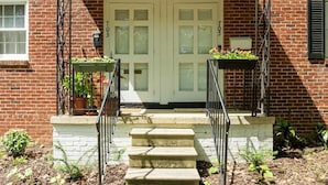 A brick building with a white front door, two steps leading up to a porch, and potted plants on either side. - Urban Escape | Near Downtown (Raleigh)