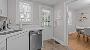 A modern kitchen with white cabinetry, a dishwasher, and a dining area with a table and chairs. - Urban Escape | Near Downtown (Raleigh)