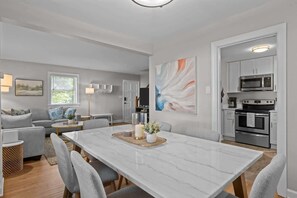 A modern living room with a marble dining table, grey sofas, and a kitchen with white cabinets and stainless steel appliances. - Urban Escape | Near Downtown (Raleigh)