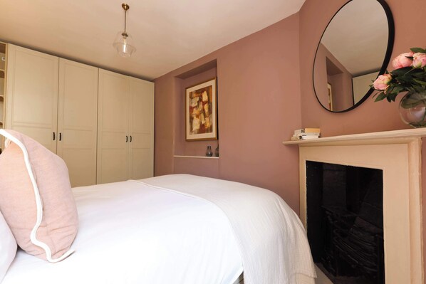 Een slaapkamer met een bed, een open haard, een spiegel en een schilderij aan de muur.