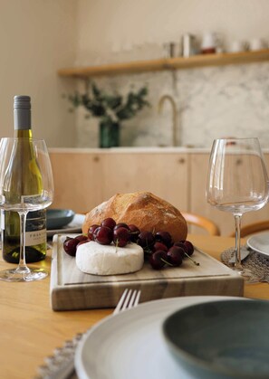Un tavolo da pranzo con una pagnotta, una bottiglia di vino, un bicchiere di vino, un piatto di formaggio e una ciotola di ciliegie.