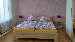 A bedroom with a bed, two bedside lamps, a hanging light fixture, and a window with a curtain.