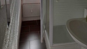 A bathroom with a shower, a window, and a radiator.