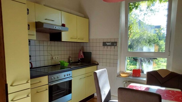 A kitchen with yellow cabinets, a stove, and a window overlooking a garden.
