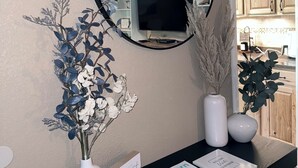 Un comptoir d’accueil avec un miroir, deux vases contenant des plantes séchées et un panneau d’accueil.