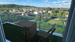 Ein Balkon mit Holztisch und -stühlen, einem Glasgeländer und Blick auf eine Wohngegend.