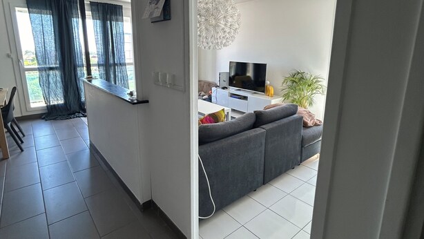 Ein modernes Wohnzimmer mit einem grauen Sofa, einem Fernseher und einer dekorativen Leuchte.