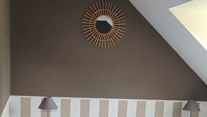 Un dormitorio con una cama grande, dos mesitas de noche con lámparas, un espejo decorativo en la pared y un techo inclinado.