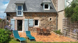 Una casa de piedra con patio de baldosas, dos sillones verdes y una mesa de madera.