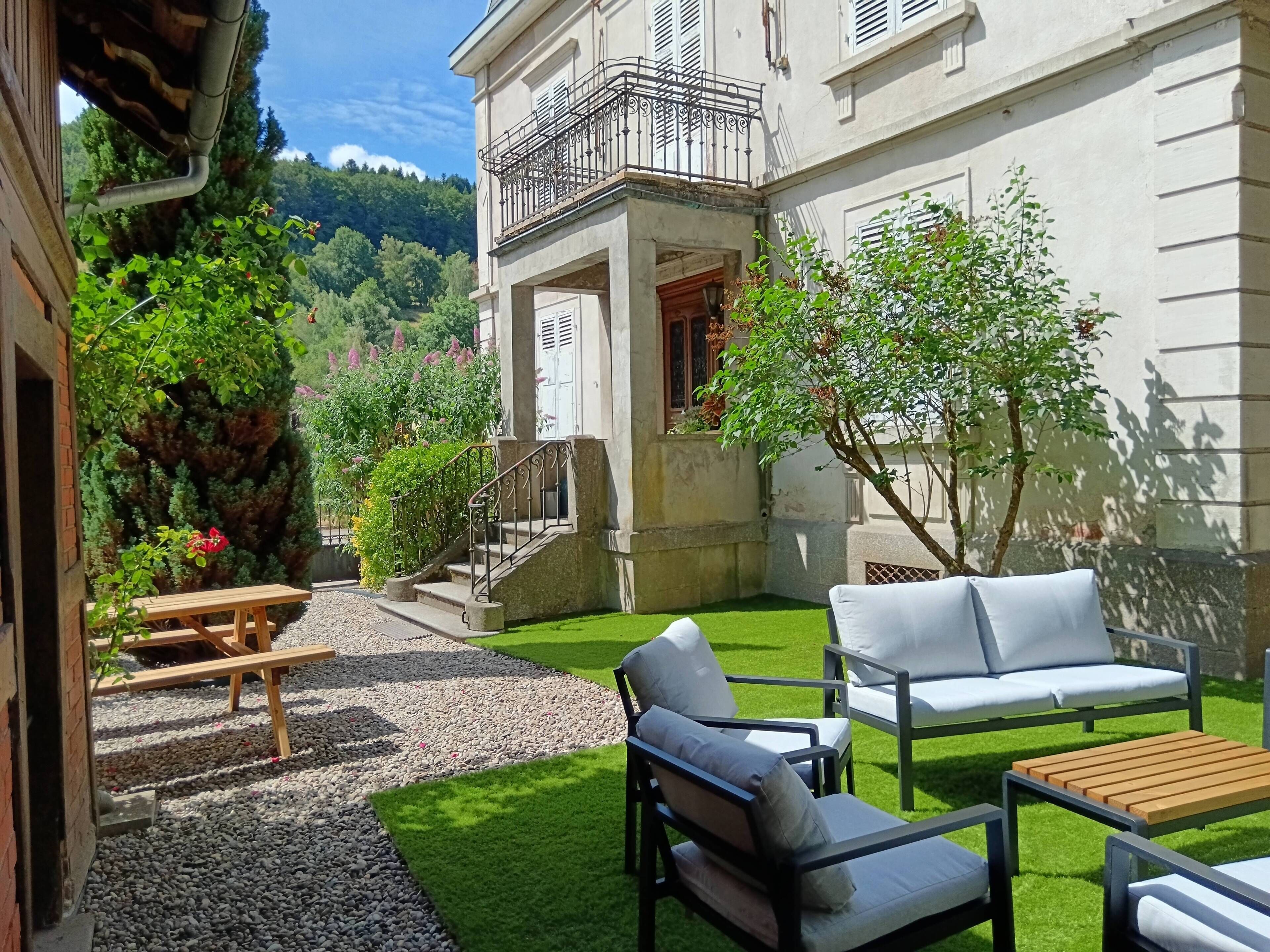 Ein Innenhof mit Gartenmöbeln, einer Treppe und Blick auf einen bewaldeten Hügel.