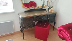 Une commode de style vintage, agrémentée d’un miroir, d’un tabouret rouge recouvert de tissu et d’objets décoratifs.