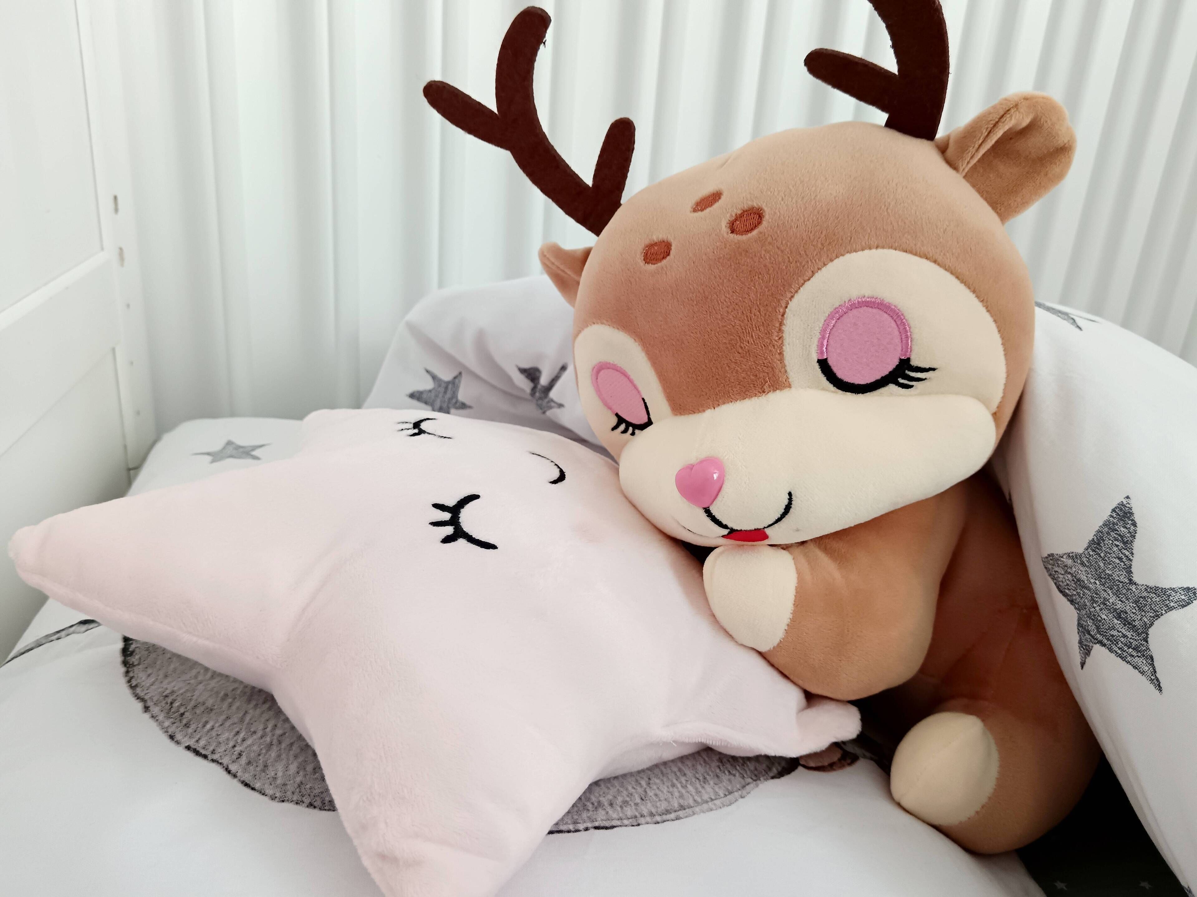 A plush toy deer with antlers resting on a pillow with a star design.