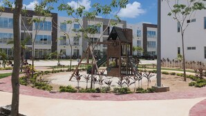 A playground with a wooden play structure surrounded by landscaped gardens and modern buildings in the background. - Close to the Turquoise Sea, ideal for couples, adventurers and families! (Cancún)