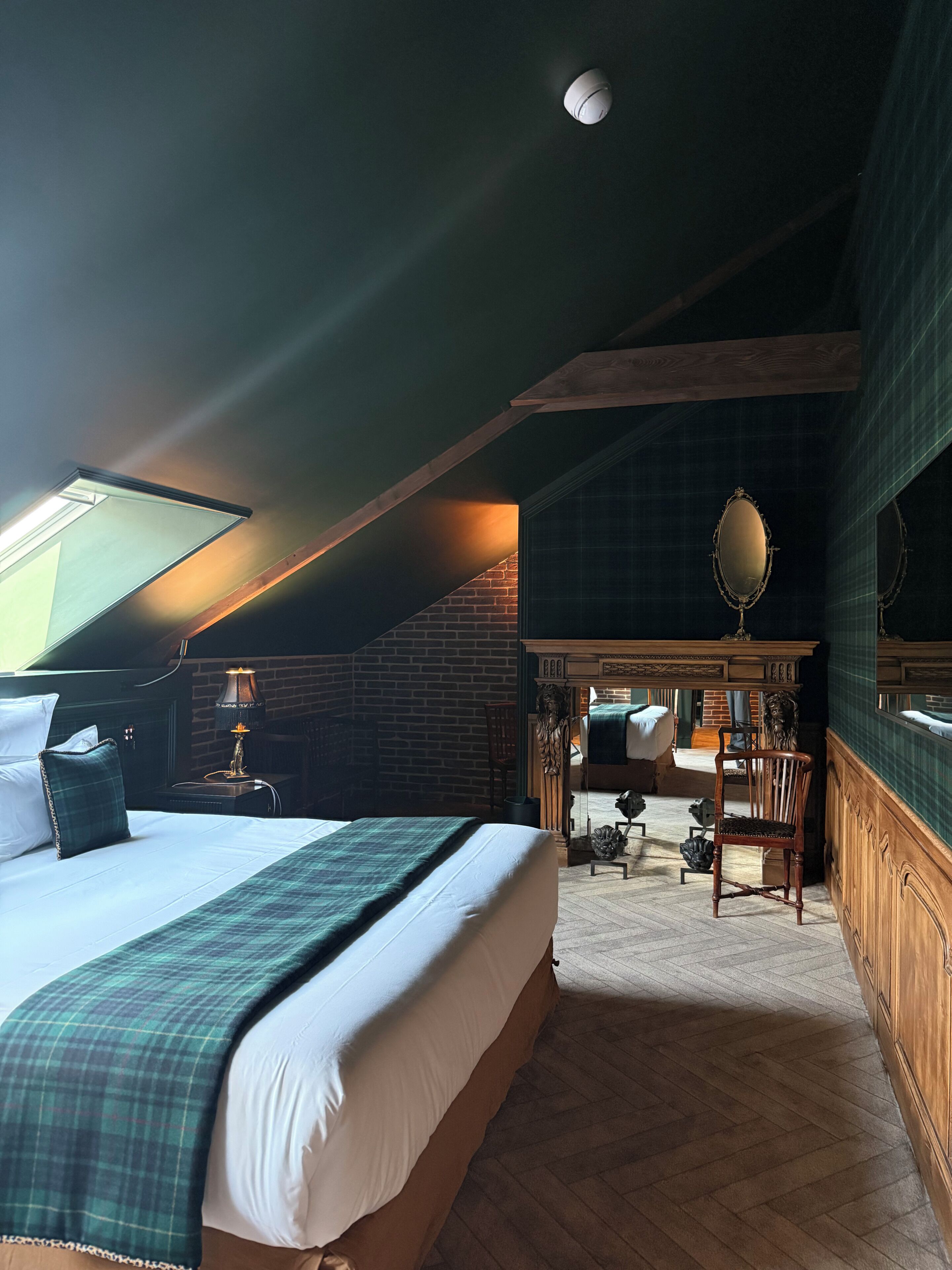 Um quarto com cama, escrivaninha, cadeira, espelho e lareira.