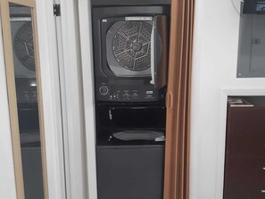 A compact, enclosed laundry room with a built-in washer and dryer, a control panel, and a small storage cabinet. - Sandelwood Studios (Nassau)