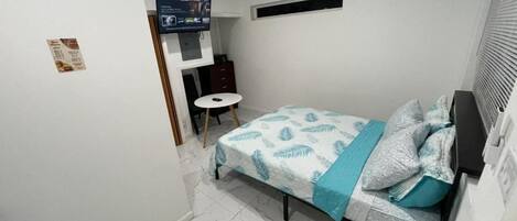 Un dormitorio con una cama, una mesita redonda pequeña, un televisor y un equipo de aire acondicionado.