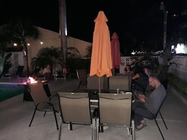 An outdoor seating area with tables and chairs, a pool, and palm trees.