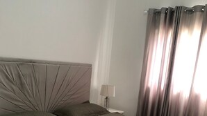 Een keurig opgemaakt bed met hoofdeinde, een bedlampje en een raam met gordijnen.