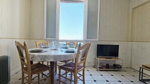 A dining area with a table set for four, chairs, a radiator, a television on a stand, and a window with a view. - Apartment: Les Senteurs de Grasse (Grasse)