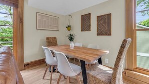 Un coin repas avec une table en bois, des chaises blanches et une plante suspendue.