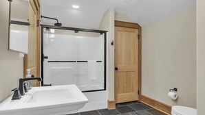 Une salle de bain avec un lavabo blanc, une douche à parois de verre, une porte en bois et des toilettes.