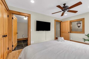 A hotel room with a bed, a ceiling fan, a flat-screen TV, wooden doors, and a wall-mounted light fixture. - 3 Min to Downtown, Game Room, King bed (Greenville)