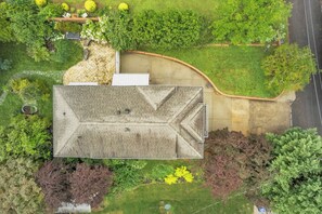 Eine Vogelperspektive eines Gebäudes mit geneigtem Dach, umgeben von einem angelegten Garten mit verschiedenen Sträuchern und Bäumen.