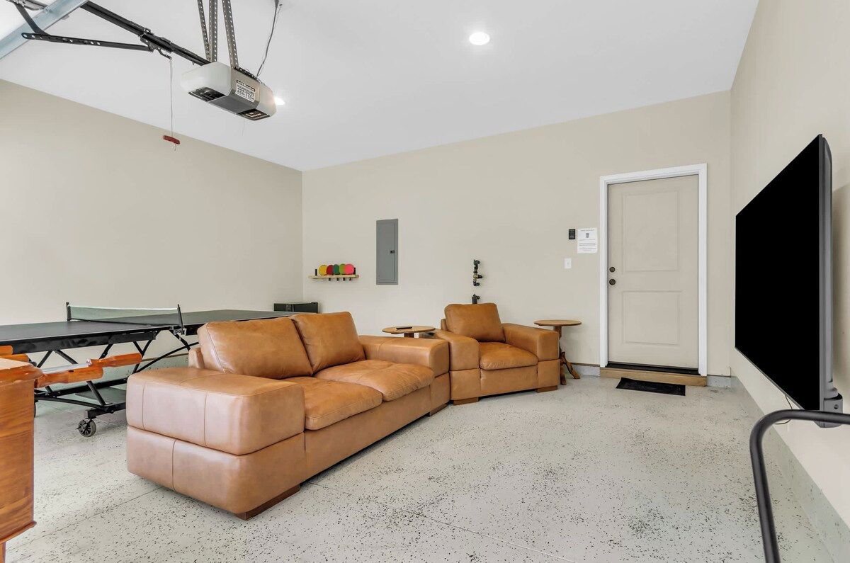 A living room with a sectional sofa, a ping pong table, a flat-screen TV, and a projector mounted on the ceiling.