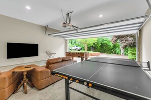 Ein Zimmer mit Tischtennisplatte, Flachbildfernseher, Sofa und einem an der Decke befestigten Projektor.