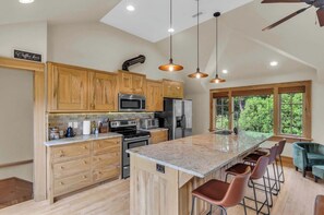 A modern kitchen with wooden cabinets, stainless steel appliances, and a large island with bar stools. - 3 Min to Downtown, Game Room, King bed (Greenville)