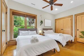 A hotel room with two beds, a ceiling fan, a window with a view of greenery, and wooden doors. - 3 Min to Downtown, Game Room, King bed (Greenville)