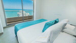 A hotel room with a large window offering a view of the sea and buildings.