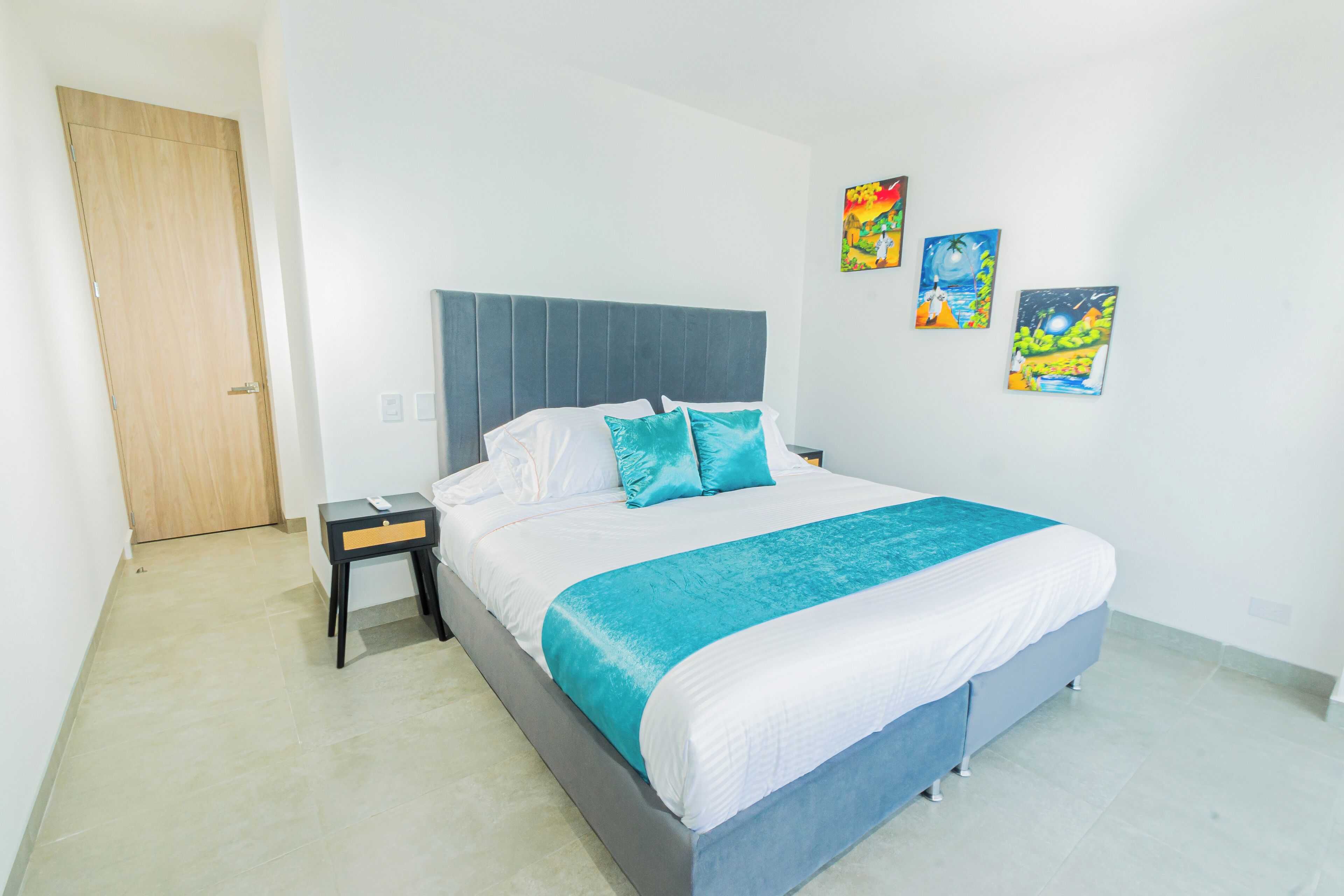 Un dormitorio con cama, mesita de noche, puerta de madera y tres adornos en la pared.