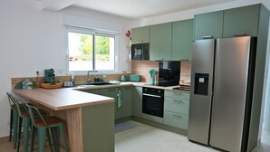 A modern kitchen with a central island, bar stools, a refrigerator, and a microwave.