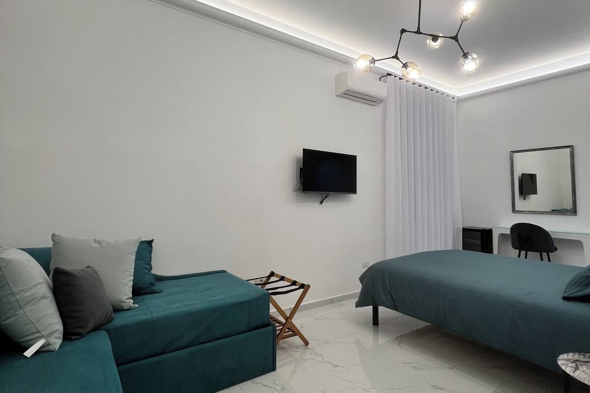 Ein modernes Schlafzimmer mit einem Türkis-Sofa, einem Bett, einem Schreibtisch und einem an der Wand montierten Fernseher.