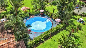 Vista aérea de un complejo turístico con una piscina central rodeada de exuberante vegetación y palmeras.