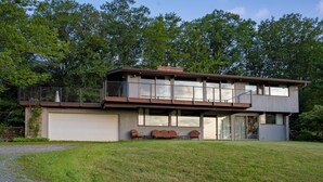 Une maison moderne à deux étages, dotée d’un garage, de grandes fenêtres et d’un espace extérieur aménagé avec un coin salon couvert.