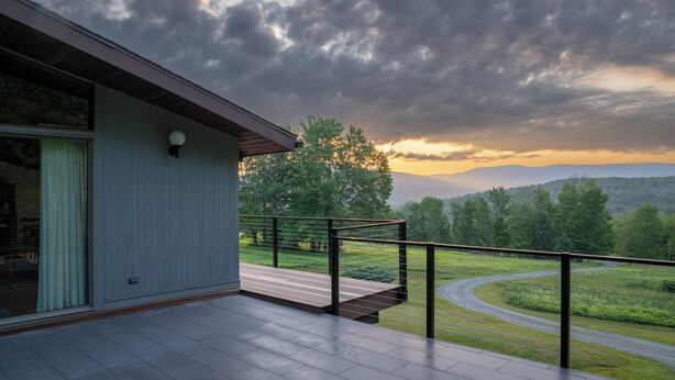 Un bâtiment moderne doté d’un balcon donnant sur une route sinueuse et un paysage luxuriant.