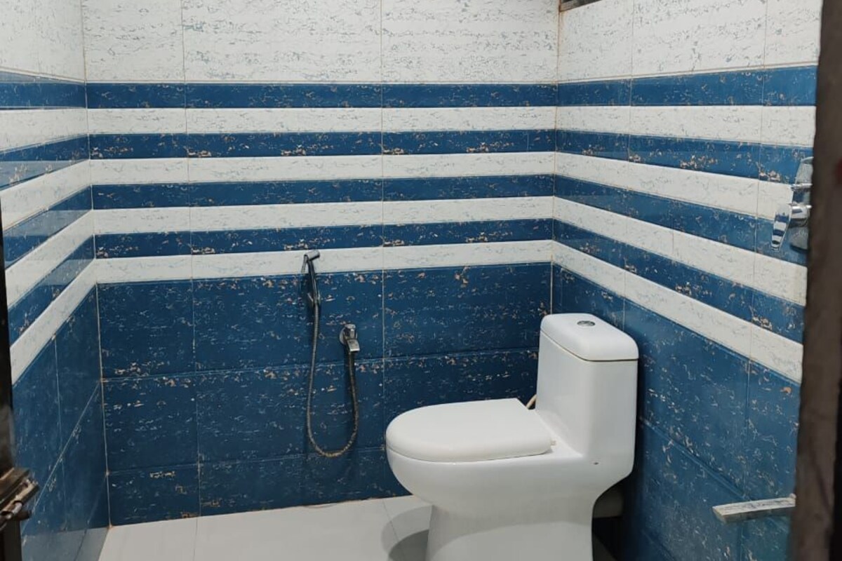 Un baño pequeño con inodoro blanco, azulejos azul y blanco a rayas, una ducha y un cubo verde.