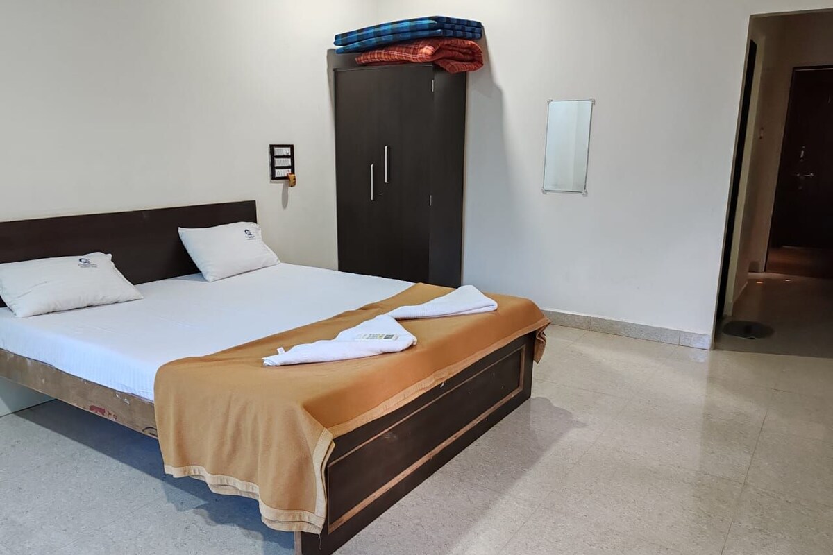 Una cama con una colcha marrón, almohadas blancas y una manta a cuadros azules y rojos.